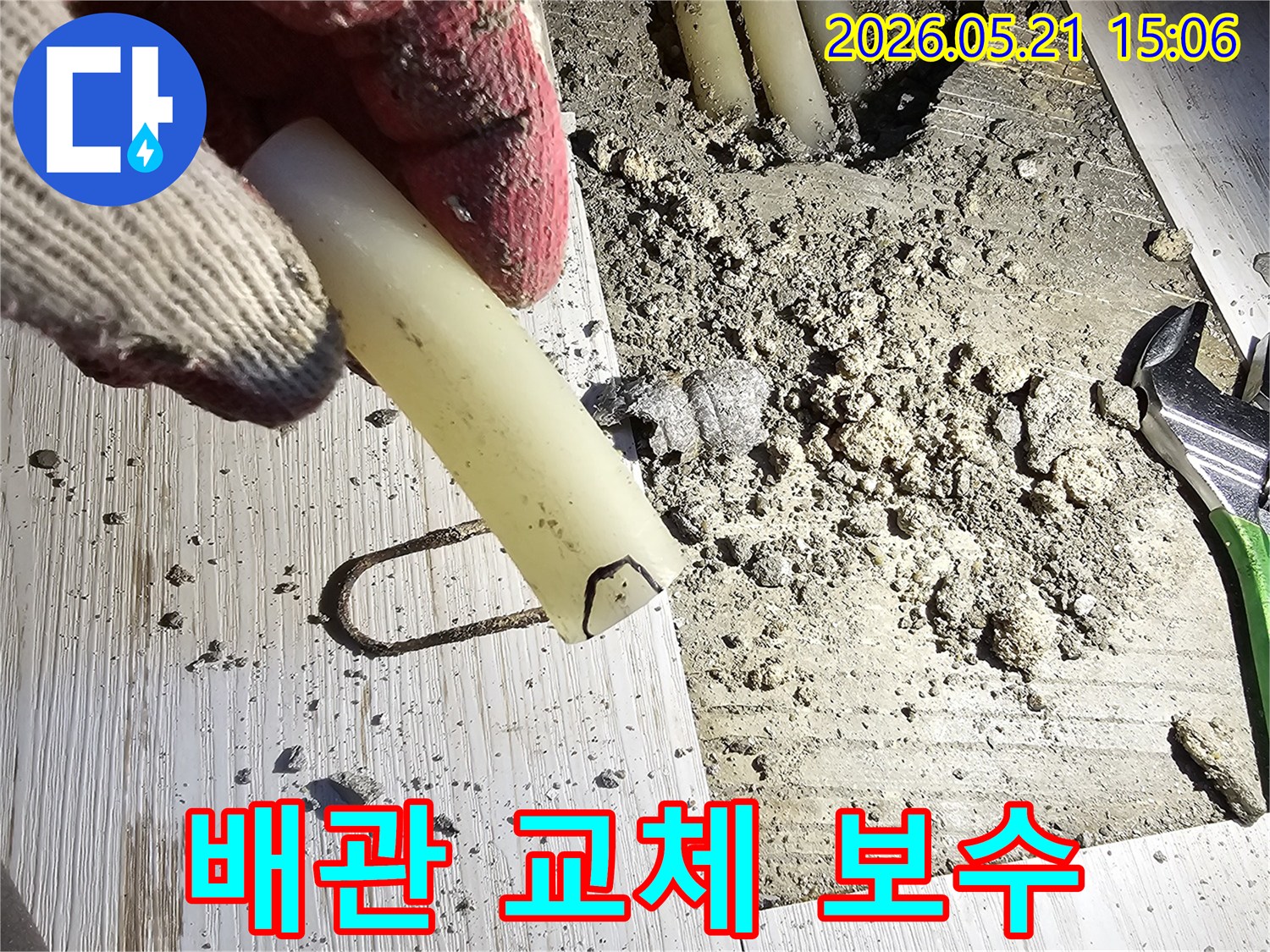 작업 장갑을 낀 손이 파손된 배관 조각을 들고-교체 및 보수 작업을 설명하는-현장 사진입니다