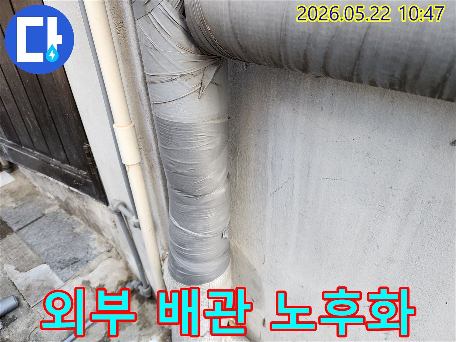 건물-외벽에-설치된-회색-배관의-보온재가-낡은-테이프로-감겨-있으며-전반적인-노후화가-진행된-모습입니다