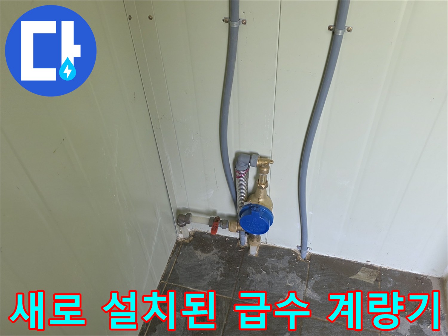 벽면에 설치된 파란색 덮개형 수도 계량기와 연결 배관