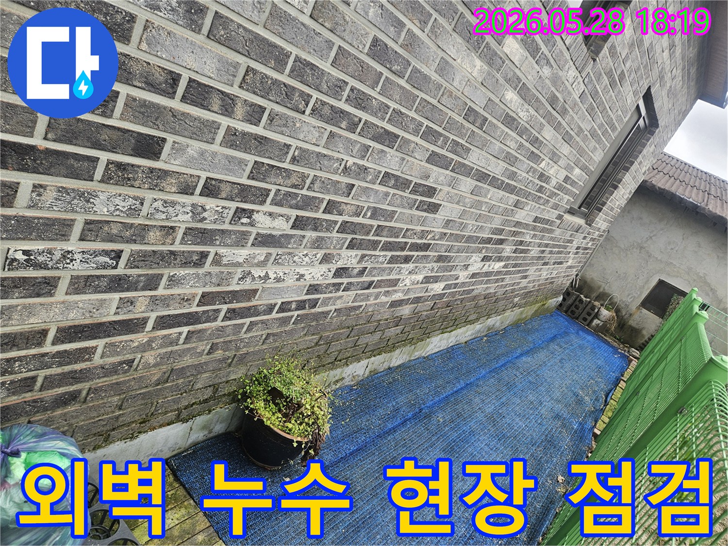회색 벽돌 외벽과-푸른색 차광막이 보이는-누수 의심 지역 현장 사진
