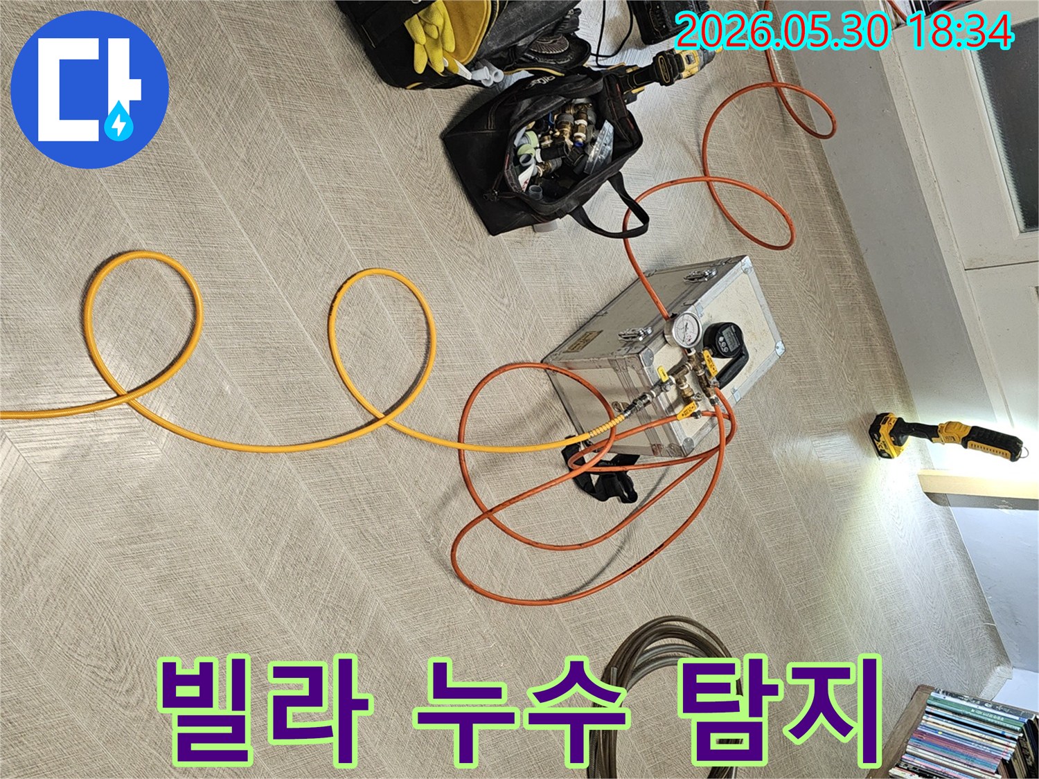실내 바닥에 설치된 누수 탐지 장비와-다양한 연결 호스-그리고 작업 도구들이-누수 진단을 위해 준비된 장면입니다.