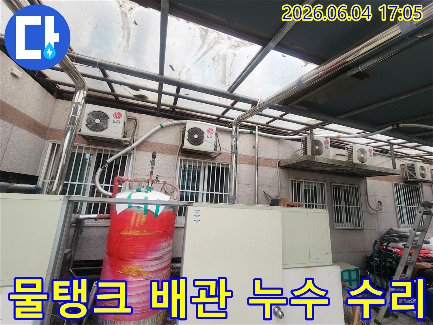 이 사진은 상가 건물 옥외에 설치된-빨간색 대형 물탱크와-그 주변의 배관들을 보여줍니다