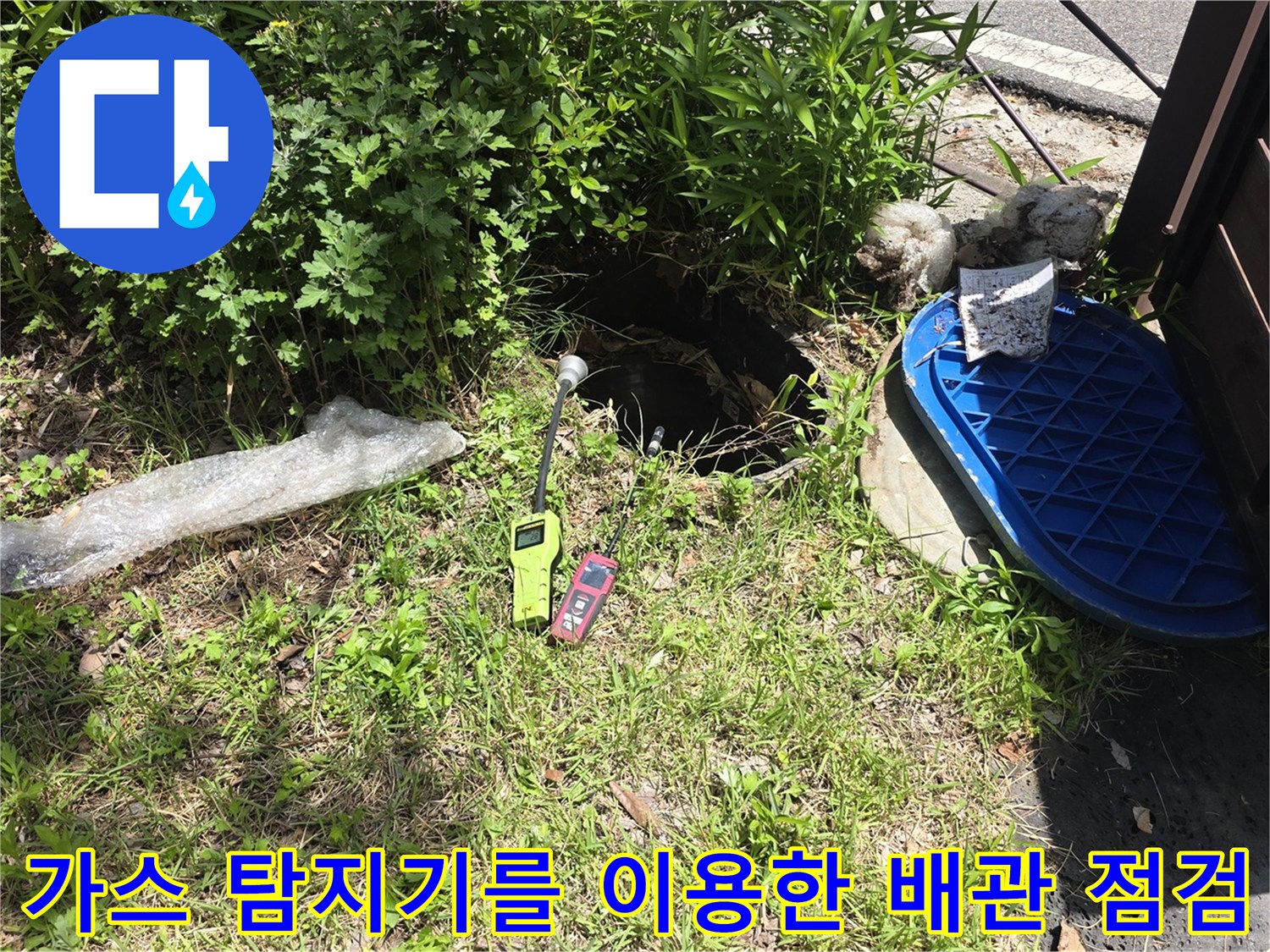 풀이 무성한 마당 맨홀 근처에서 가스식 탐지기로 누수를 찾는 장면입니다.