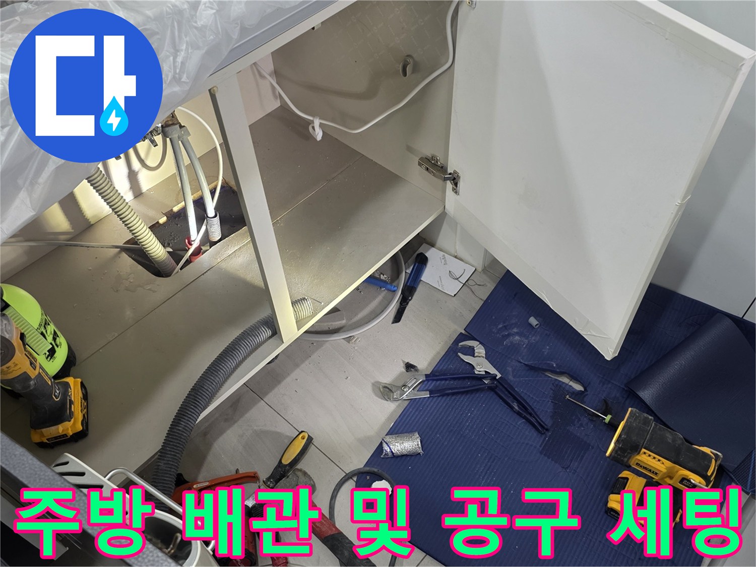 싱크대 내부의 배관 연결부와 바닥에 놓인 작업용 전동드릴