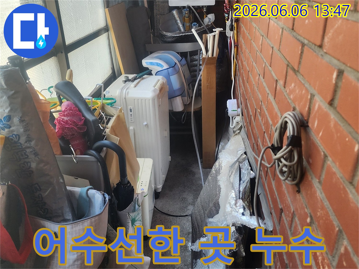 벽돌-벽-아래-복잡하게-얽힌-배관과-생활-용품들-사이에서-발견된-누수-흔적을-보여주는-사진
