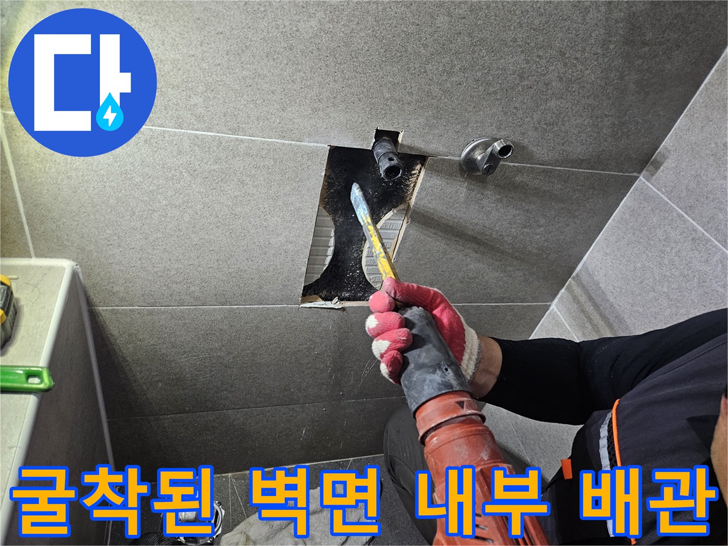 타일이 깨져 나간 자리 사이로 보이는 수도 배관과 작업용 장비입니다.