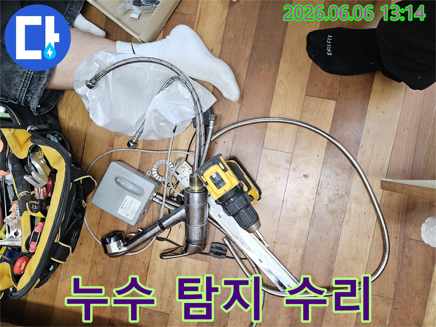 누수 공사를 위해 준비된 다양한 배관 부품과-전문가용 전동 드릴-그리고 공구 가방이 바닥에 놓여 있는 모습입니다.