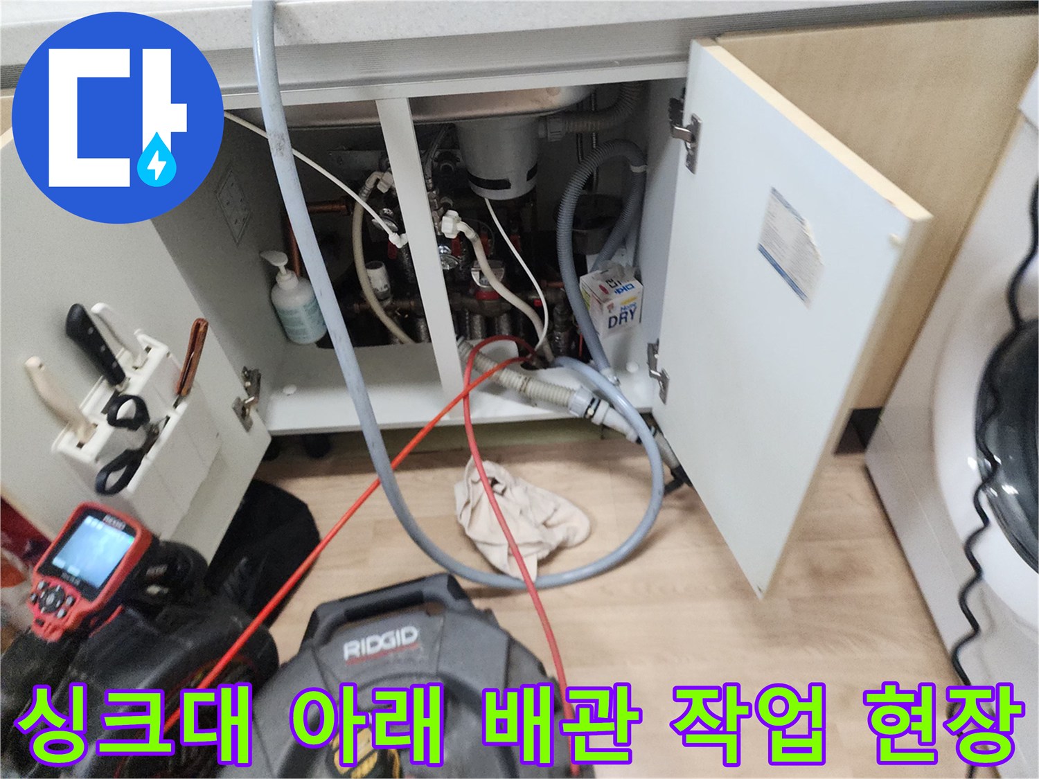 싱크대 하부장 내부의 복잡한 배관과 바닥에 놓인 청소 장비