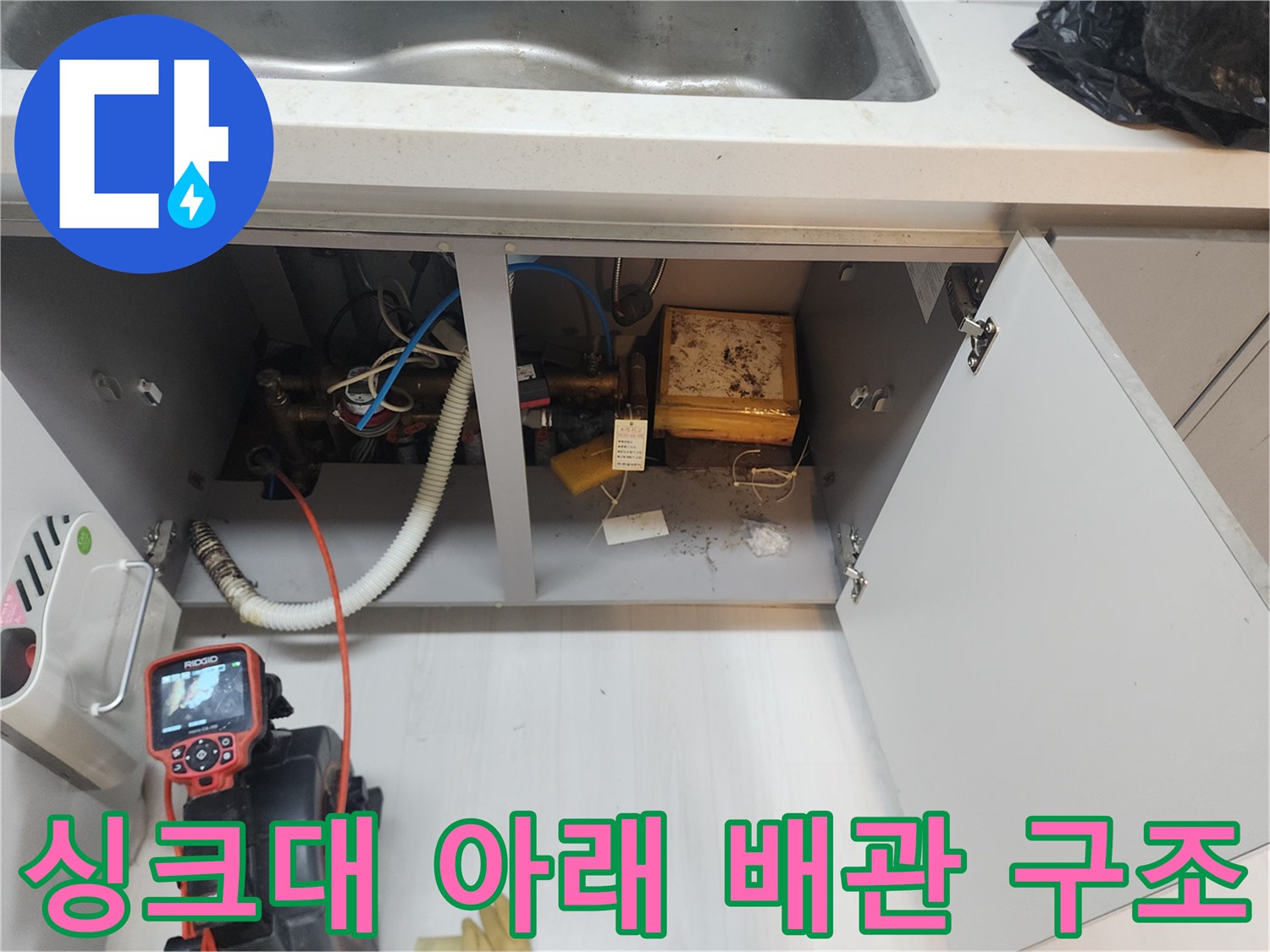 싱크대 하부장 내부에 연결된 굵은 배관과 점검용 장비의 모습