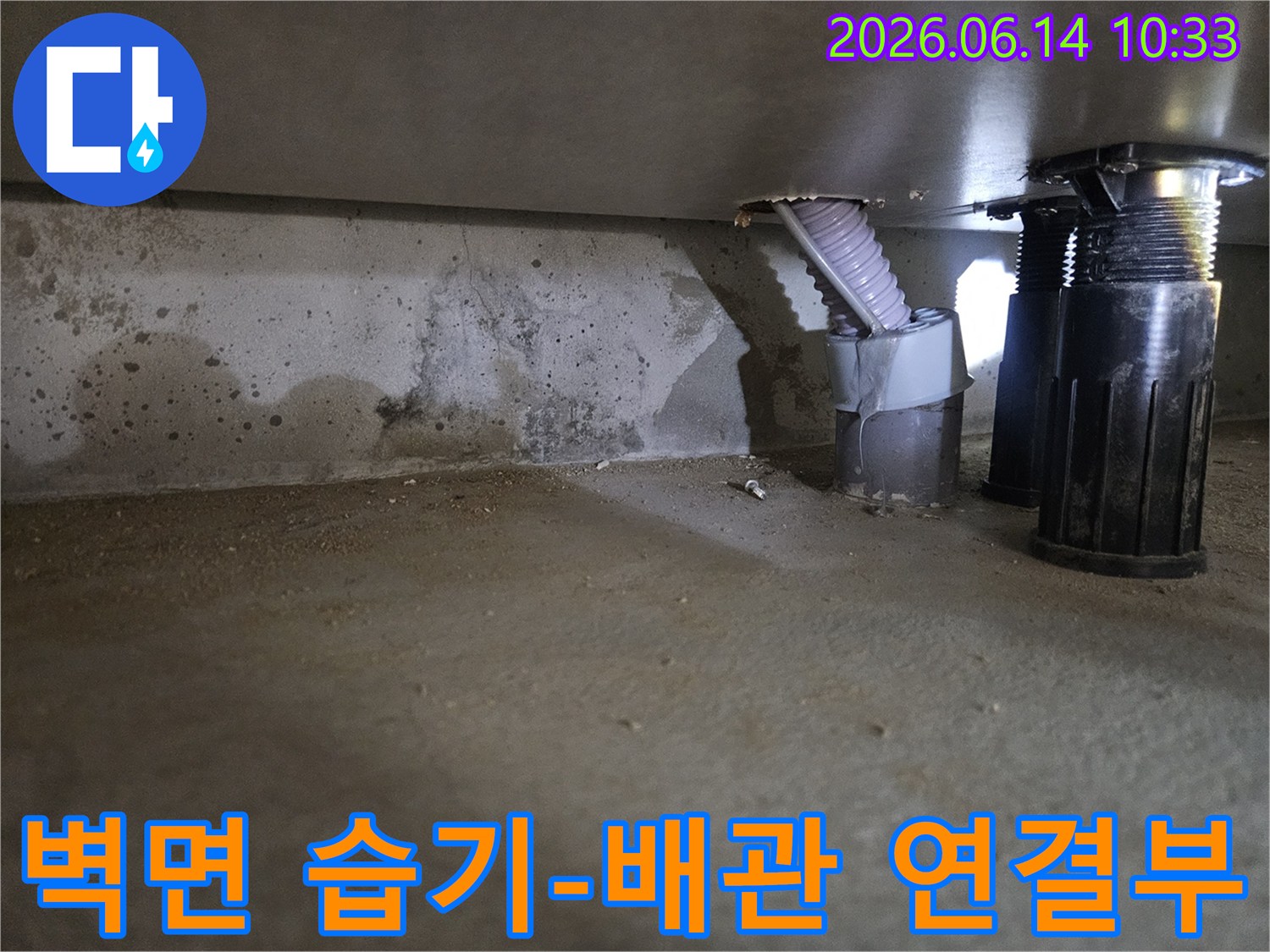이 사진은 콘크리트 벽면의 습기와-그 옆에 위치한 배관 연결부의 상태를 보여줍니다.
