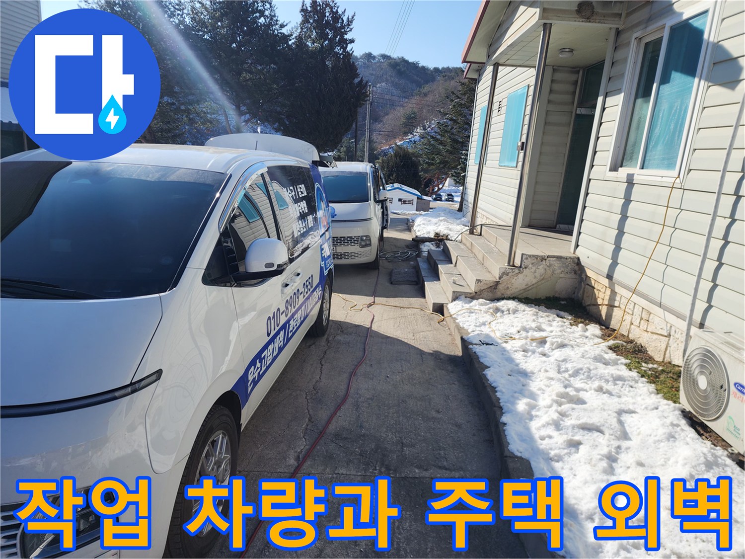 배관 세척 장비를 갖춘 흰색 작업차량과 주택 건물 사이의 모습