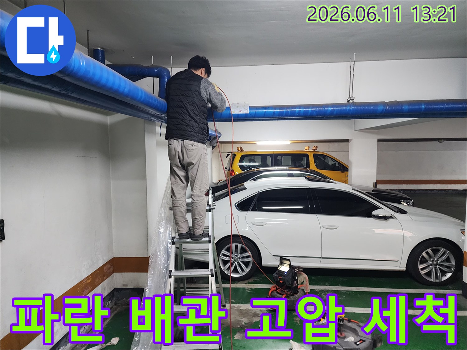 사다리 위에서 파란색 대형 배관의 이물질을 제거하는 작업 현장입니다.