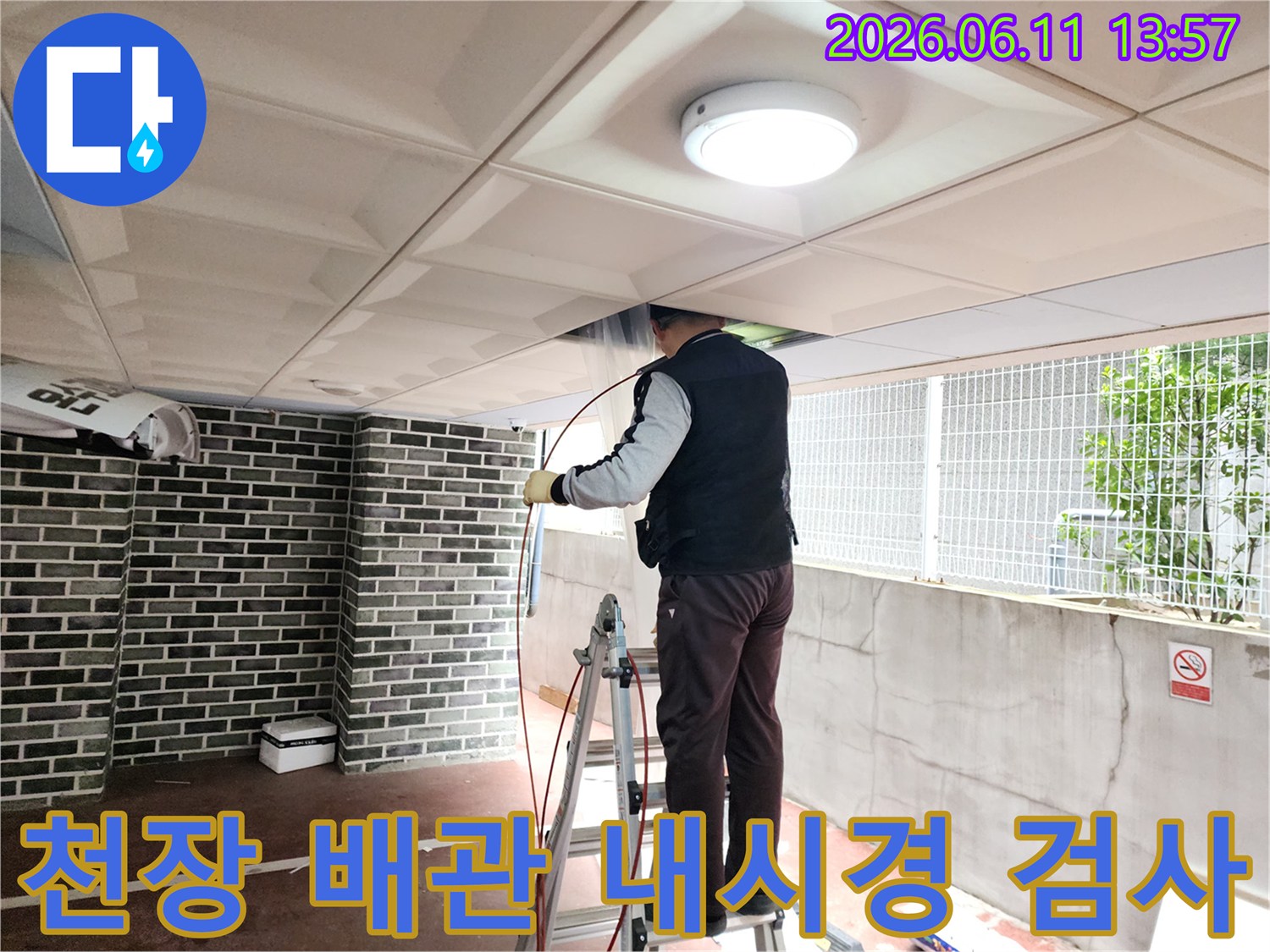 사다리 위에서 천장 점검구를 통해 배관 내부를 확인하는 엔지니어의 모습입니다.