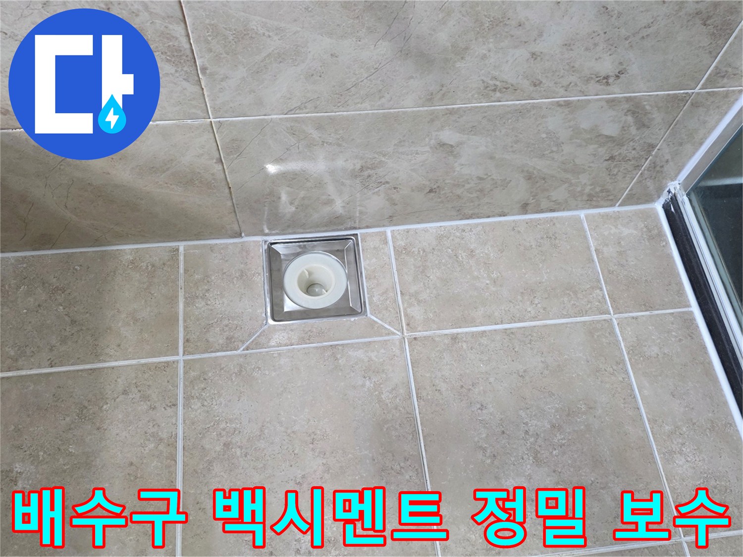 베이지색 타일 바닥에 설치된-사각형 금속 배수구의 모습으로-주변 백시멘트의 마감 상태를 보여줍니다