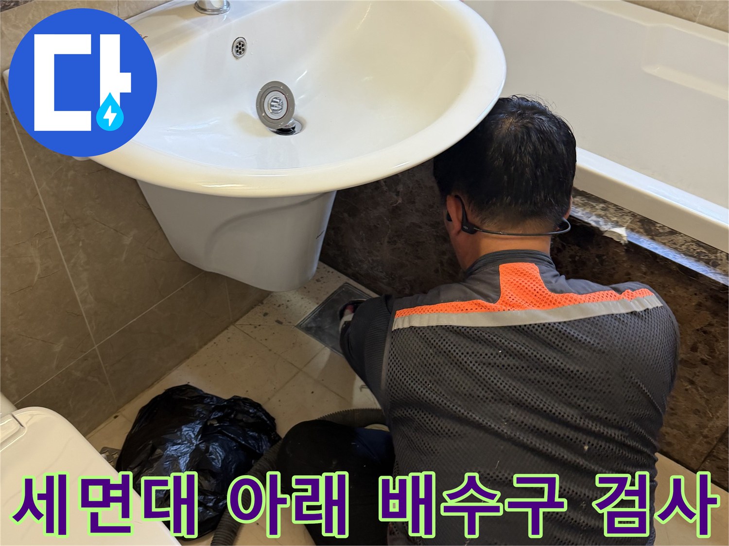 엔지니어가 세면대 밑바닥의 배관 연결 부위를 자세히 살피고 있습니다.