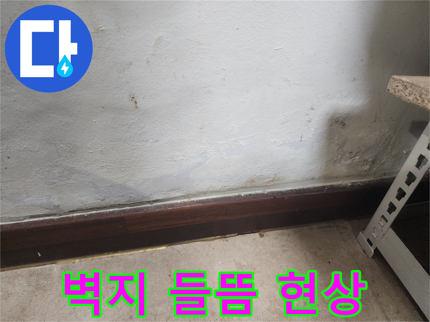 벽 하단부에 물이 스며들어 벽지가 젖고 곰팡이가 피어있는 누수 피해 현장 사진입니다.