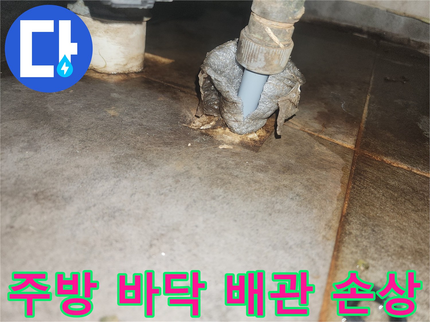 이 이미지는 주방 바닥을 뚫고 지나가는 배관 주변의-심각한 누수 손상과 부식 상태를-명확하게 보여줍니다.