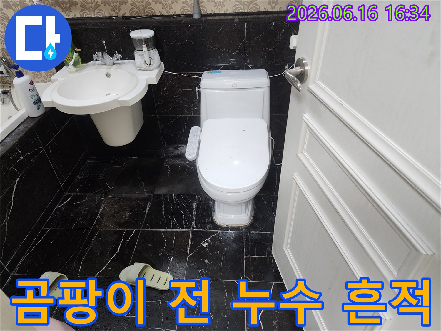 검은색 대리석 무늬 타일 바닥에-하얀색 변기가 놓여있고-그 주변으로 물이 고여 말라붙은-흔적이 보이는 욕실 사진입니다.