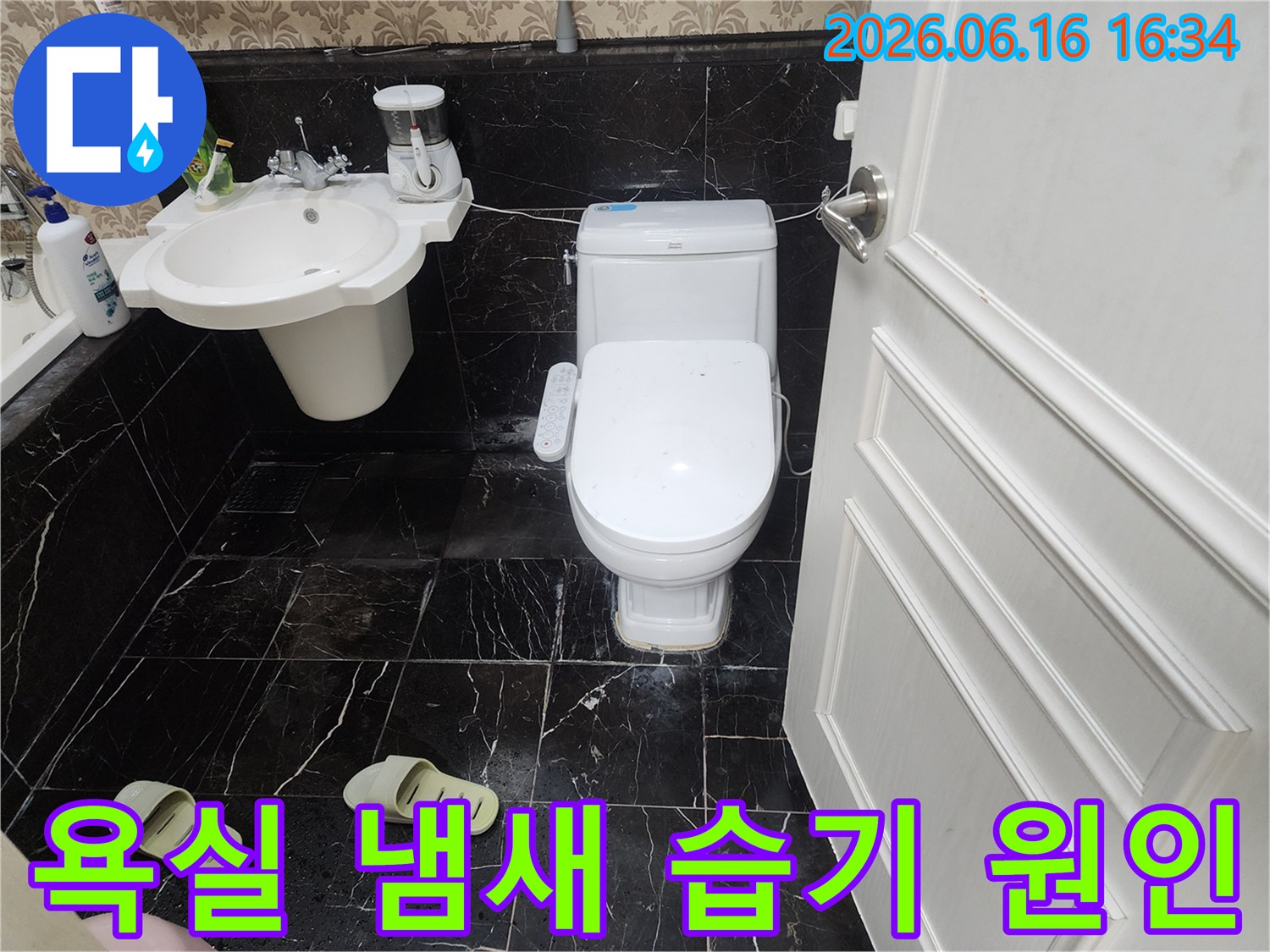 검은색 타일 바닥 위에 놓인-하얀색 변기 주변에-하얀색 물때 자국이 선명하게 보이는-욕실 내부 사진입니다.