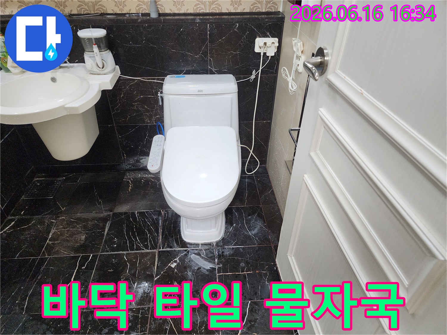 화장실 변기 하단부-검은색 타일 바닥에-물기가 번져있는-누수 현장을 촬영한 이미지입니다.