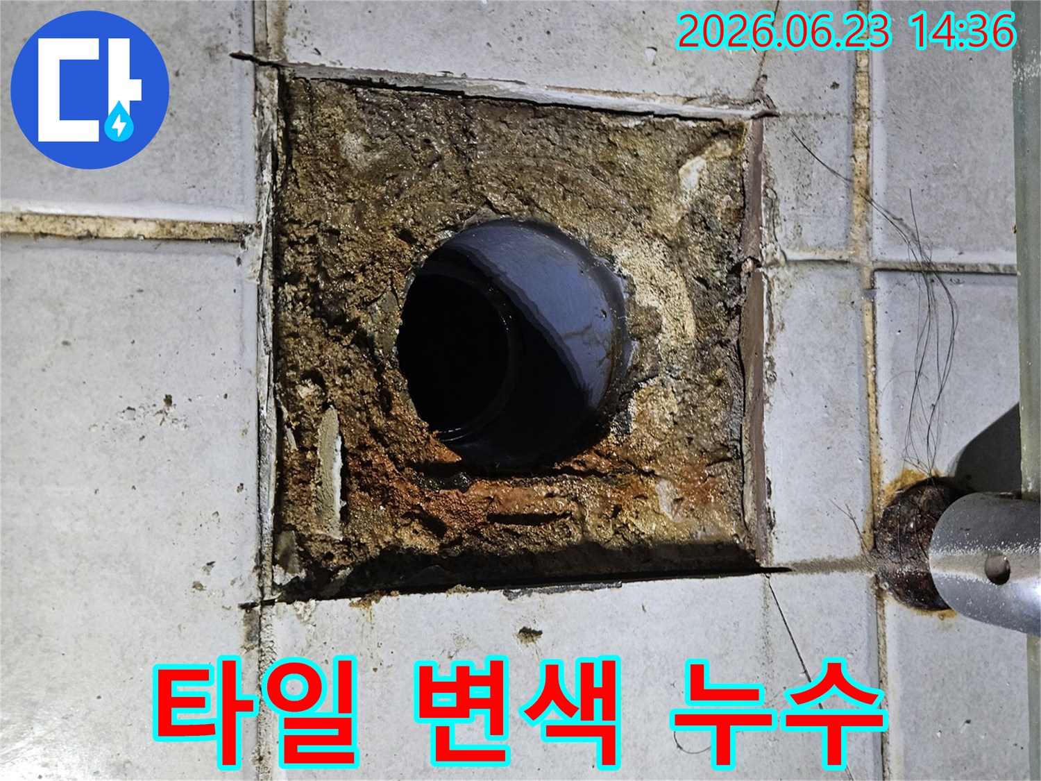 배관 주변의 바닥 타일이 누수로 인해 변색되고-손상된 모습을 보여주는 이미지