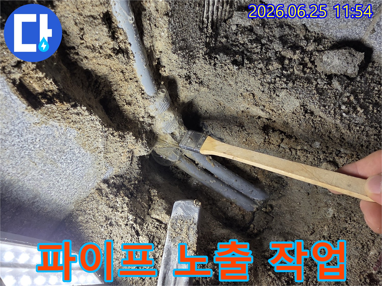 숙련된 기술자가 파묻힌 배관을 드러내기 위해 흙을 털어내는-정밀 누수 탐지 작업 현장입니다