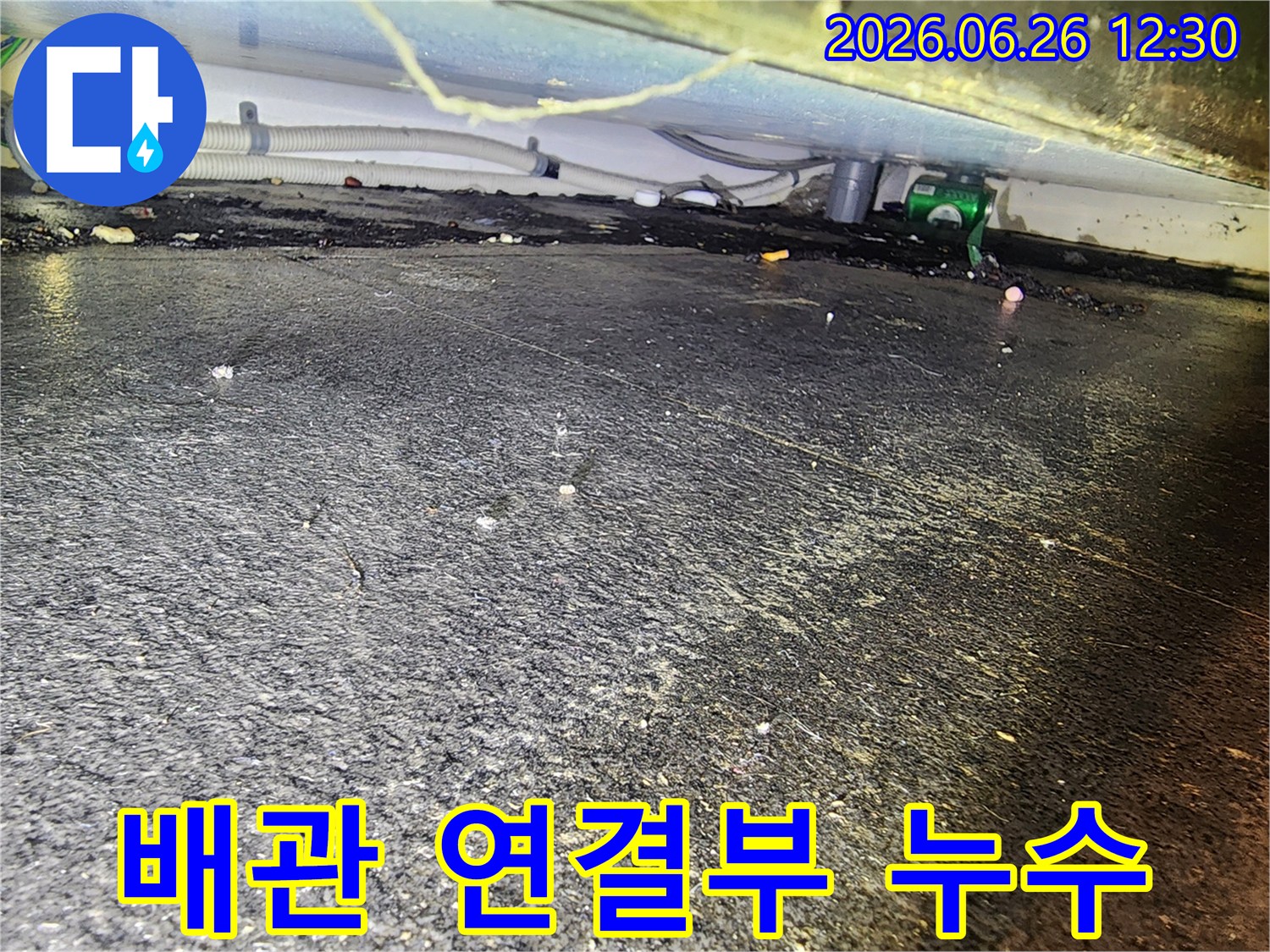 배관 연결부 근처-바닥에 고인 물과-흙먼지가 섞인-누수 현장을 촬영한 사진입니다