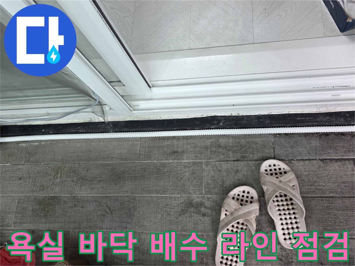 화장실 바닥 타일 경계에 놓인 하얀색 배수 호스 사진