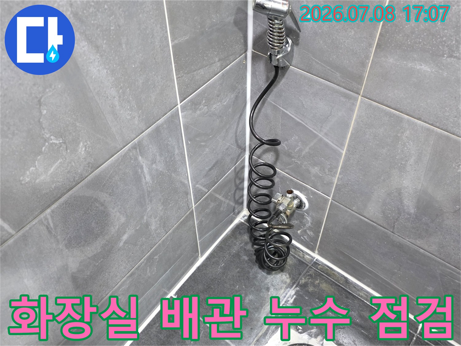 회색 타일이 시공된 화장실 바닥의 하수 배관과 노출된 코일 케이블을 촬영한 사진입니다.