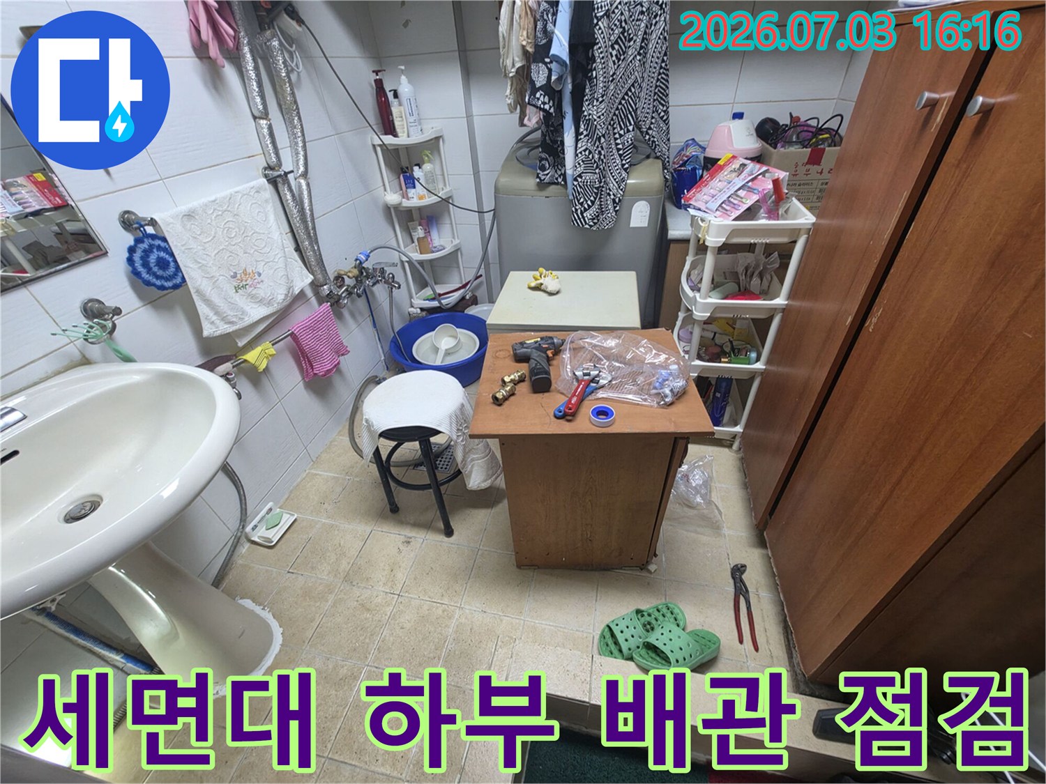 세면대 아래 노출된 배관과 주변 도구들이 있는 화장실 현장