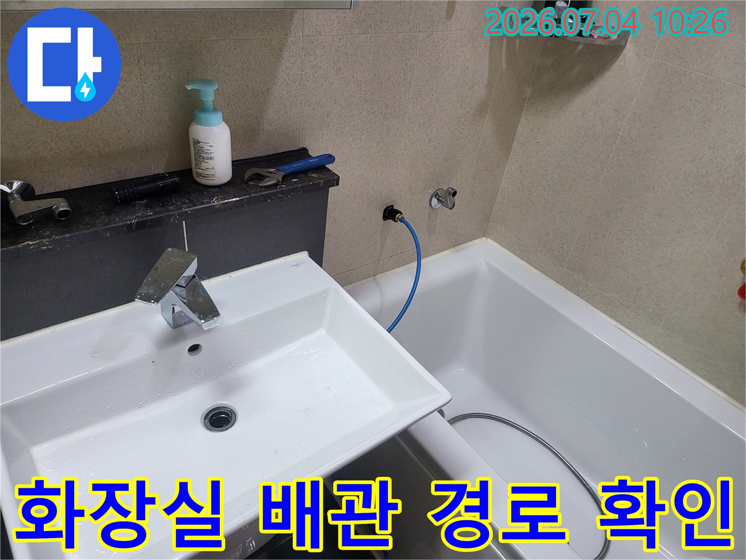 세면대 옆 파란색 호스와 노출된 수도 배관 라인을 점검하는 모습