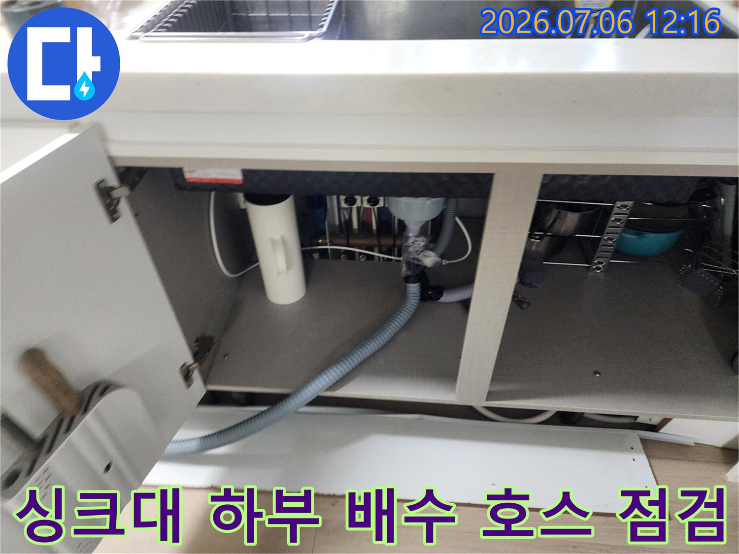 주방 싱크대 아래 노출된 회색 배수 호스의 연결 부위와 상태를 꼼꼼히 확인하는 모습입니다.