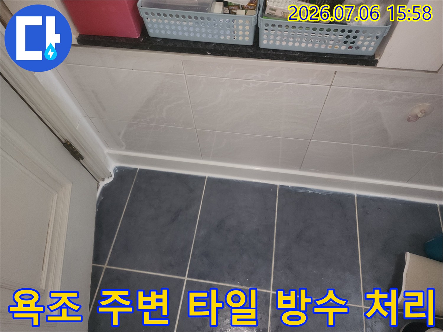 욕조와 인접한 벽면의 흰색 타일과 바닥의 어두운 색 타일이 만나는 지점의 방수 처리 상태