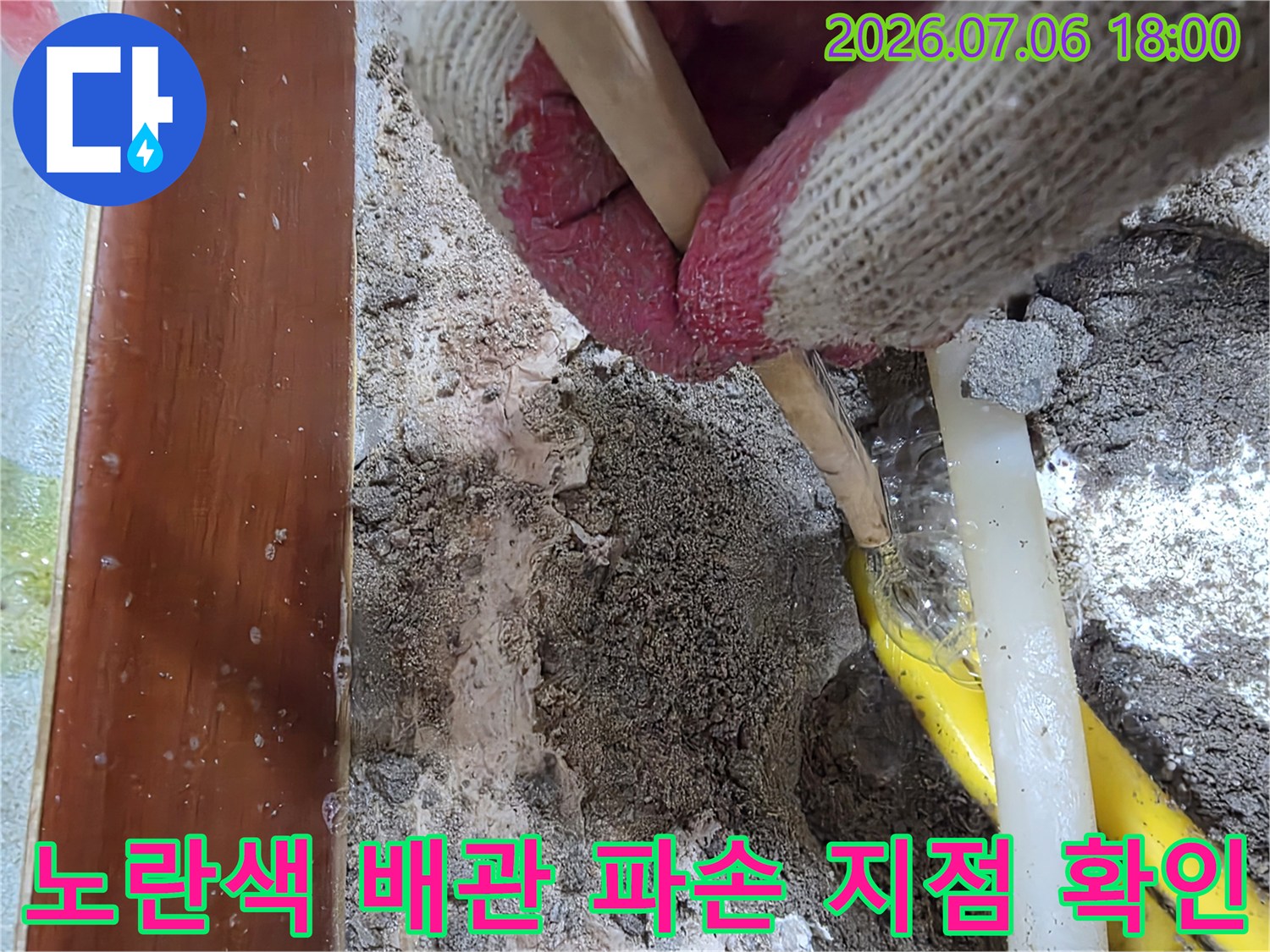 장갑을 낀 작업자가 노란색 배관의 파손 부위를 손가락으로 가리키는 모습