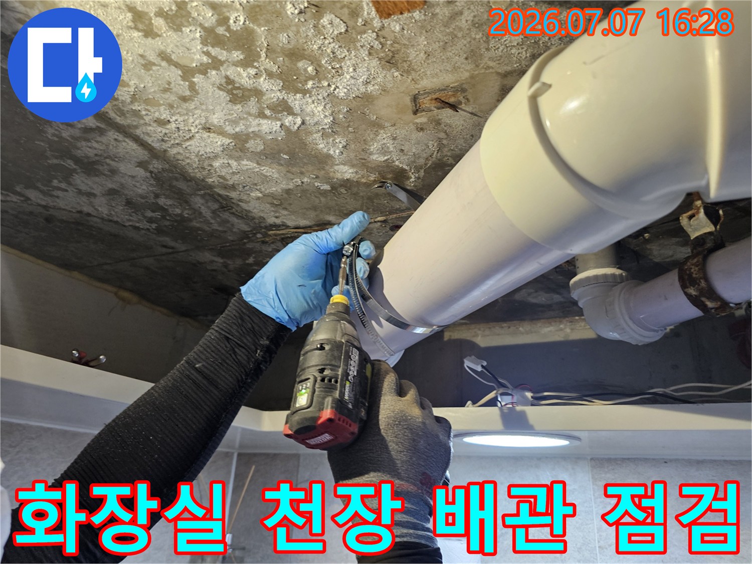 작업자가 파란 장갑을 끼고 화장실 천장 내 노후된 배관 연결 부위를 확인하며 작업하는 모습