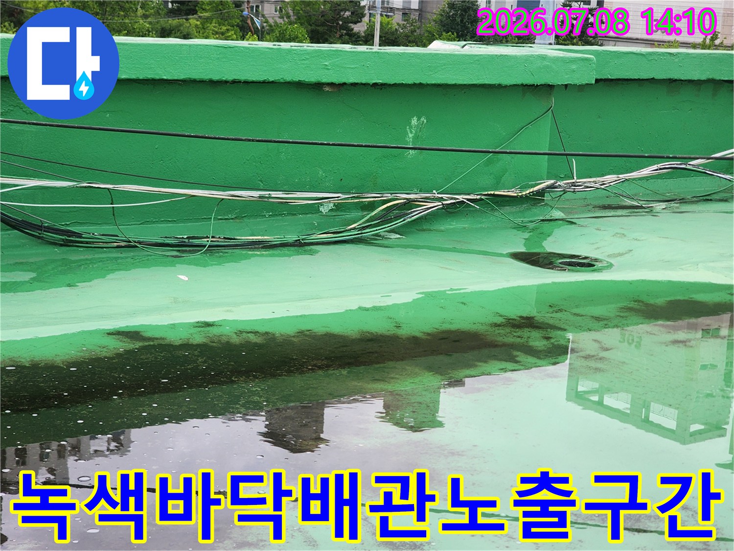 초록색 바닥에 여러 선과 파이프가 지나가는 옥상 공간