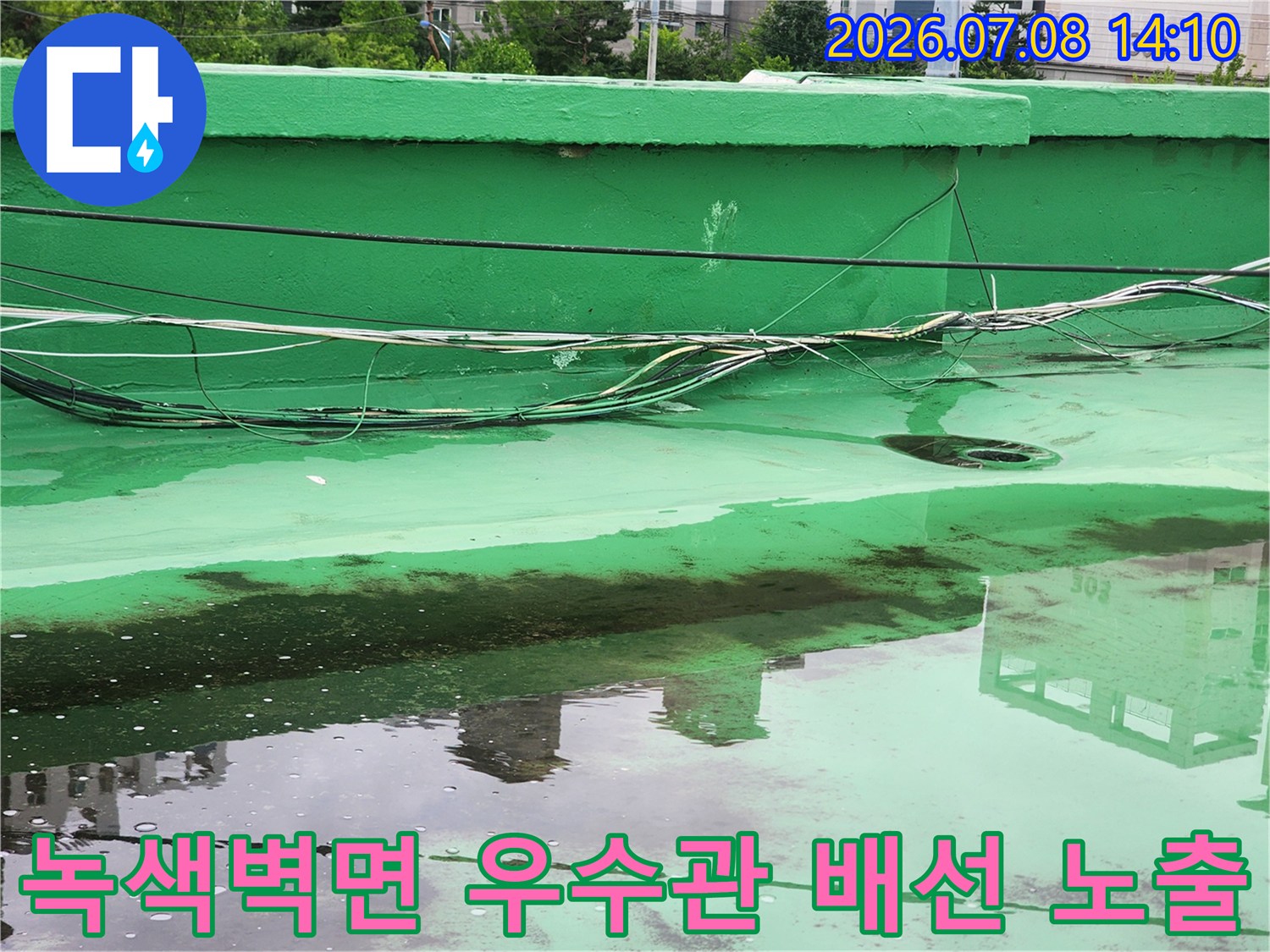 초록색 벽면에 복잡하게 얽힌 전선과 관이 지나가는 베란다 외벽 모습