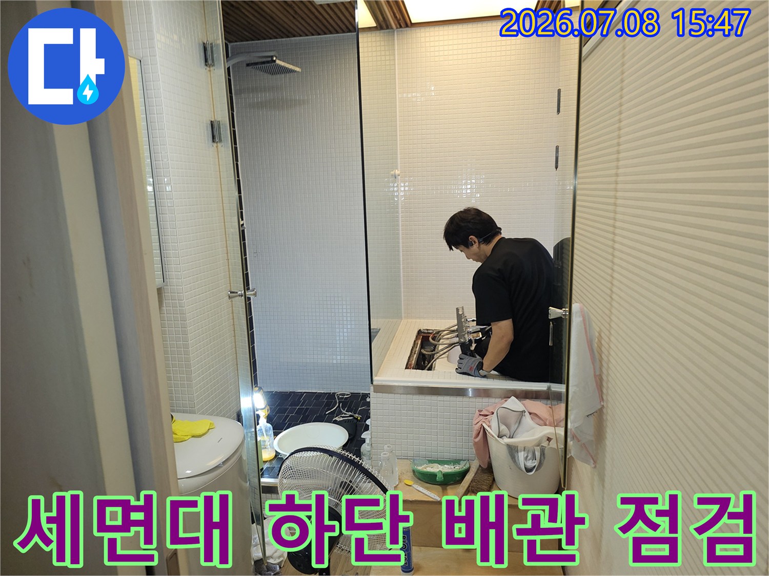 전문가가 화장실 세면대 아래 배관 연결부를 조사하는 장면