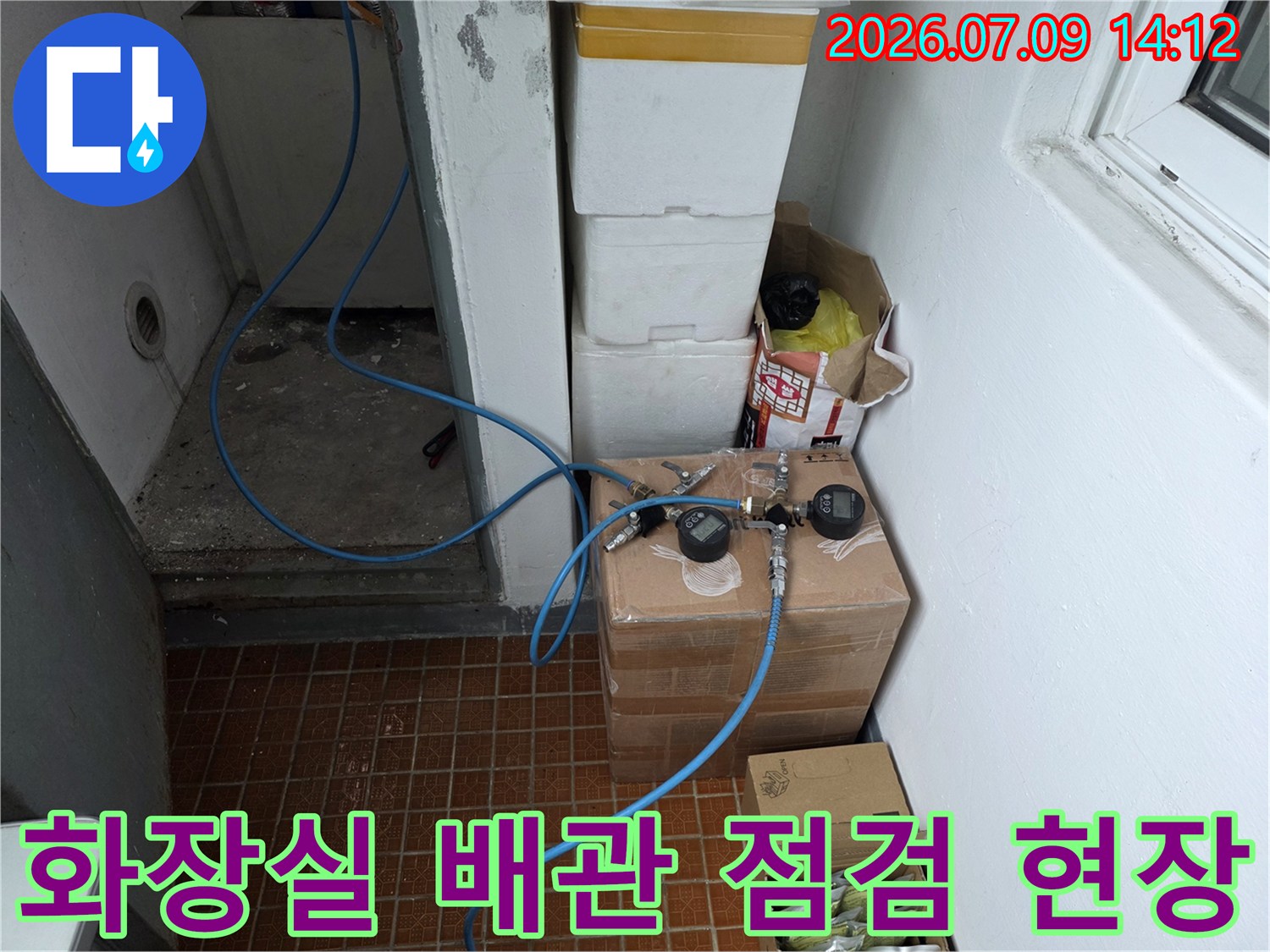 화장실 내부에서 노출된 수도 계량기와 파란색 호스가 연결된 배관 시스템을 점검하는 모습