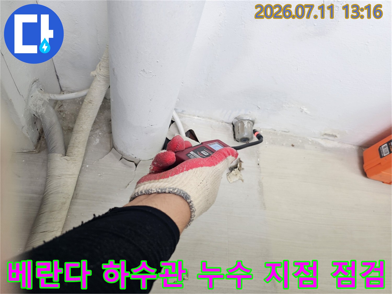 작업자가 장갑을 끼고 렌치를 사용하여 베란다 바닥 배관 연결 부위를 정밀하게 점검하는 모습