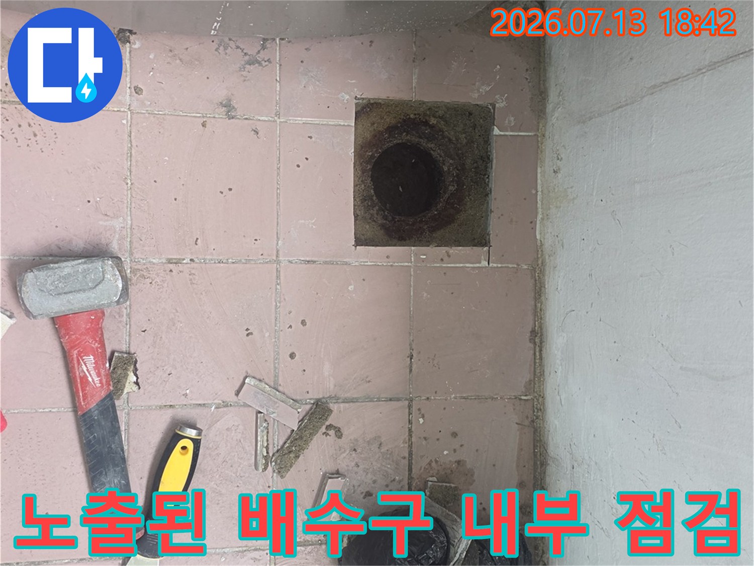 파손된 타일 주변의 배수 트랩과 내부에 노출된 배관 구조