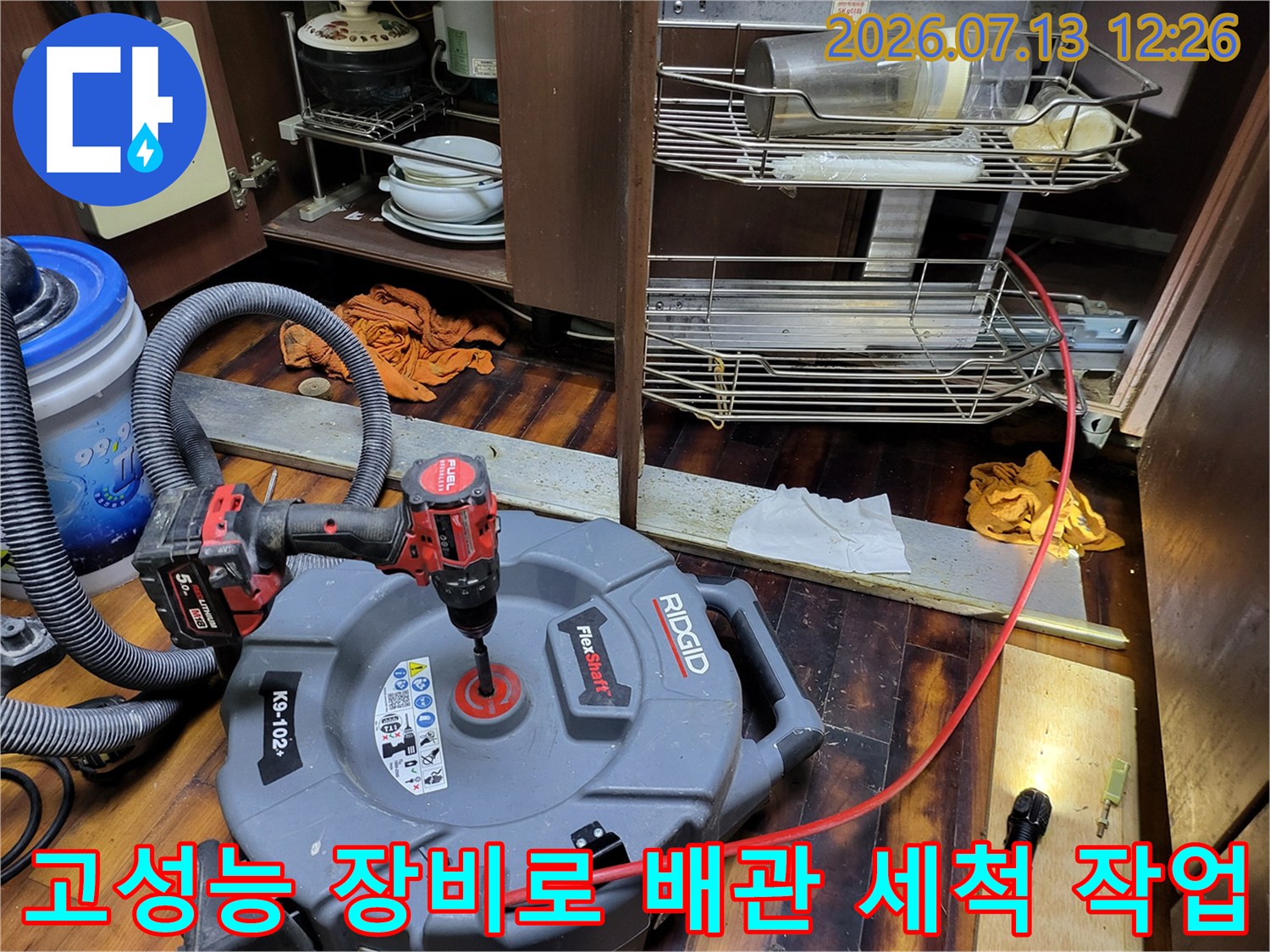 싱크대 밑에 설치된 대형 청소 장비를 연결하여 배관 내부를 클리닝하는 모습