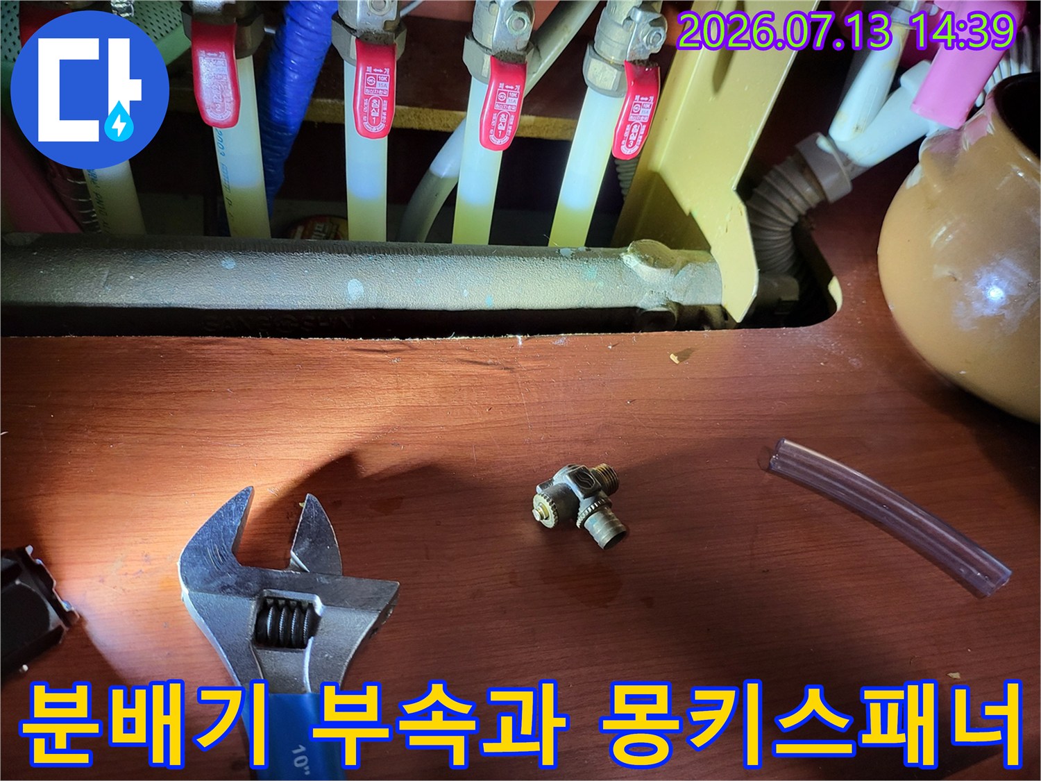 누수 수리를 위해 분리한 황동색 배관 부속과 조절 렌치-몽키스패너가 놓여있는 모습