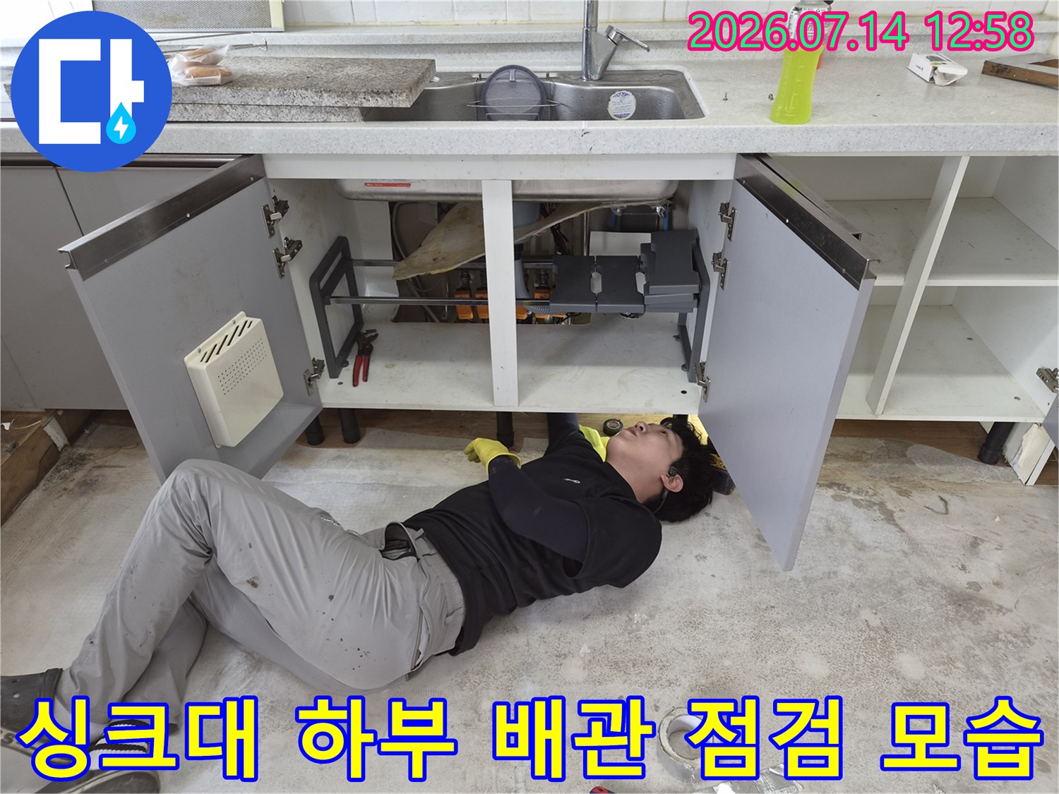 작업자가 싱크대 아래 좁은 공간에 누워-배관 상태를 확인하는 모습