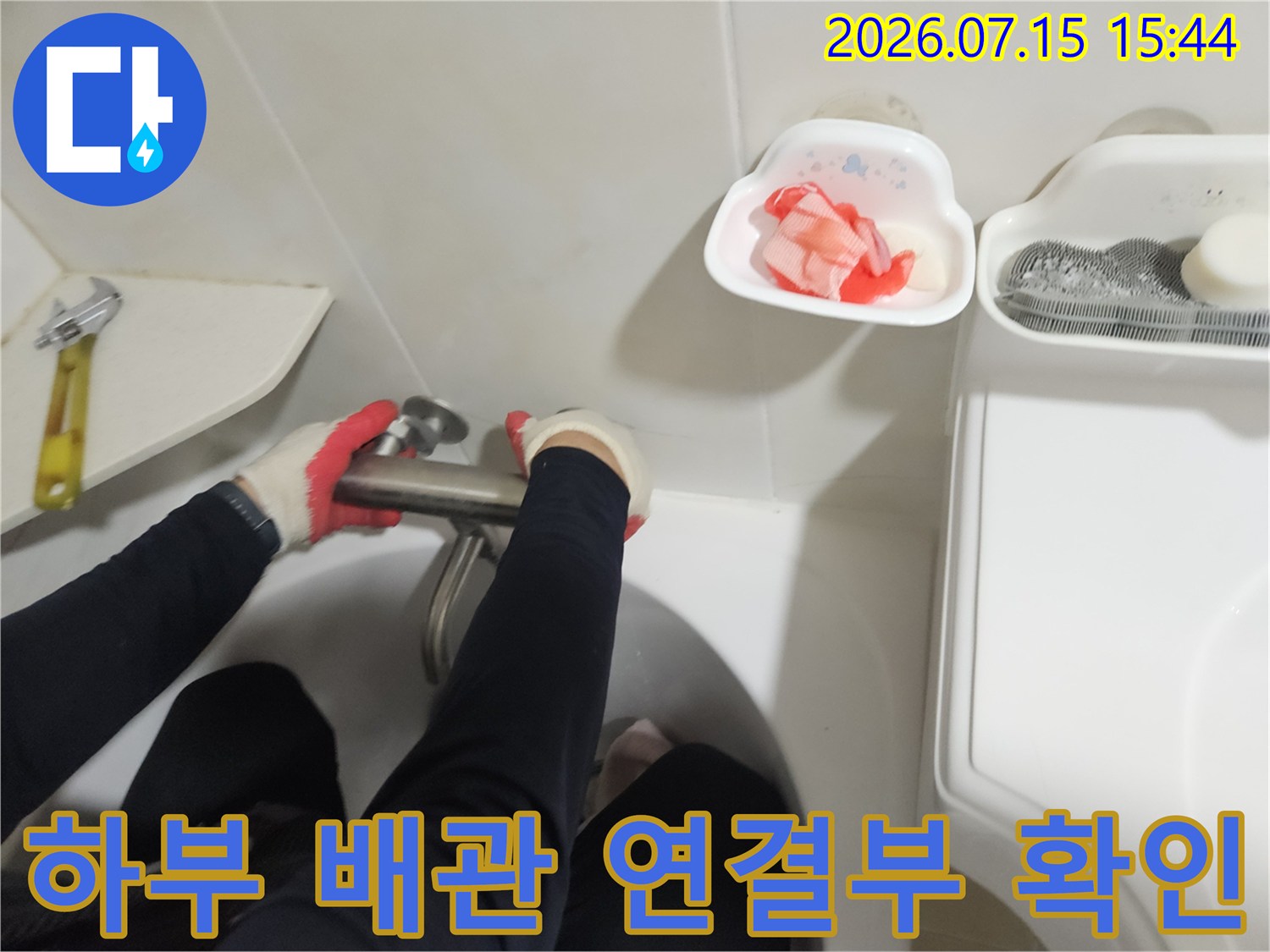 작업자가 장갑을 끼고 세면대 밑 파이프를 점검하는 모습