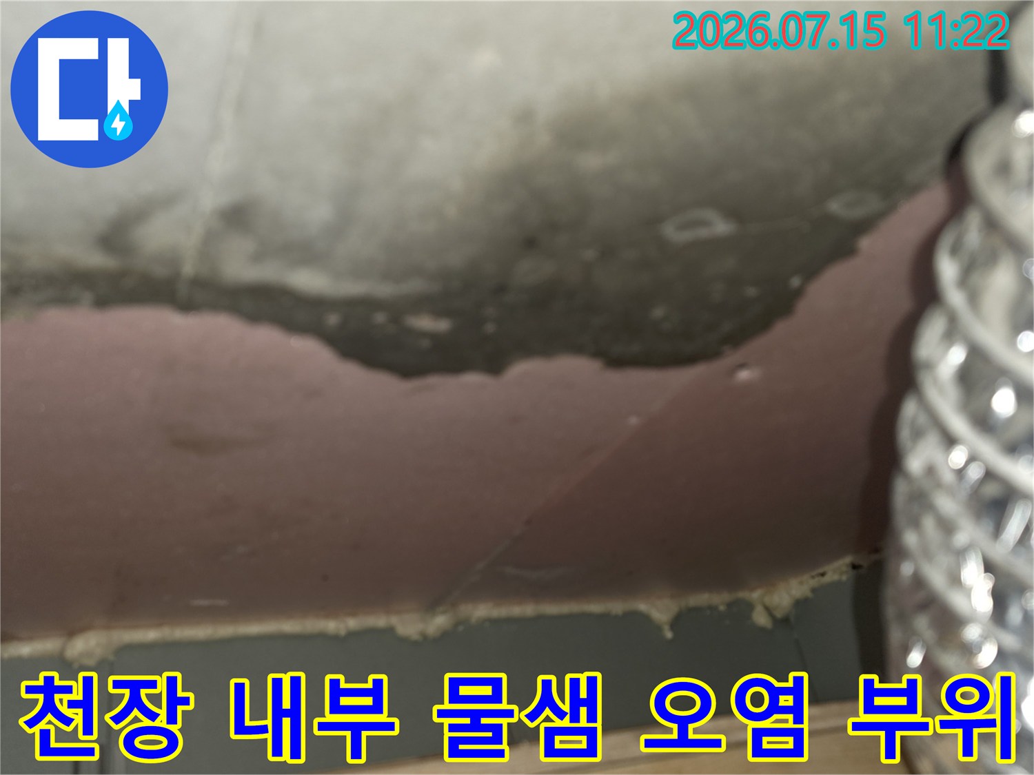 은색의 유연한 배관-그 뒤편 천장에 나타난 짙은 색의 누수 얼룩