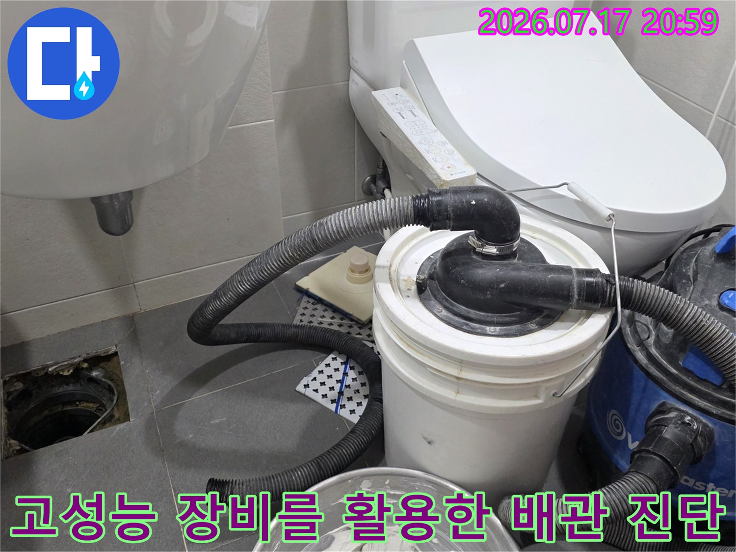 화장실 바닥의 누수 원인을 찾기 위해 대형 흡입기와 내시경 카메라를 연동하여 점검하는 과정입니다.