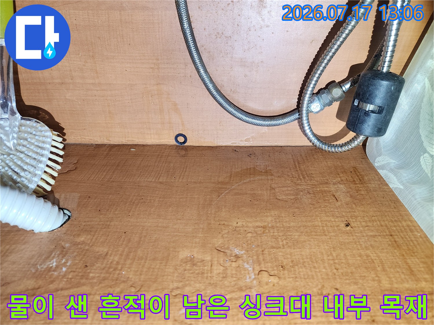 습기로 인해 색이 변한 주방 하부장의 나무 벽면-금속 및 플라스틱 배관 호스들