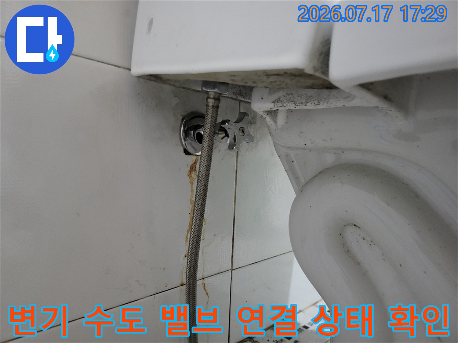 양변기와 벽면 배관을 이어주는 은색 금속 밸브와 호스의 체결 모습