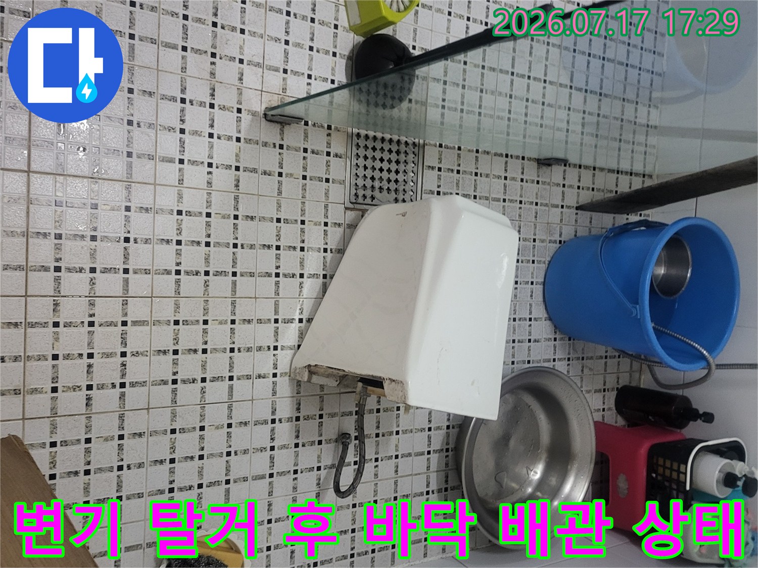 화장실 바닥 타일 위에서-변기가 탈거되어 내부 연결 부위와 호스가 드러난 모습